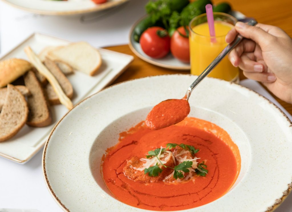 stainless steel spoon in tomato soup on white ceramic plate